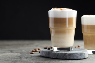 Photo of Tasty latte macchiato in glasses and coffee beans on grey table, closeup. Space for text