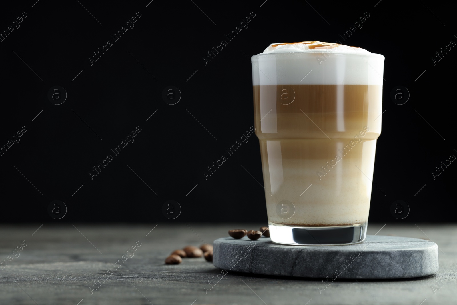 Photo of Tasty latte macchiato in glass and coffee beans on grey table, closeup. Space for text