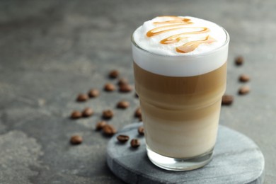 Photo of Tasty latte macchiato in glass and coffee beans on grey table, closeup. Space for text