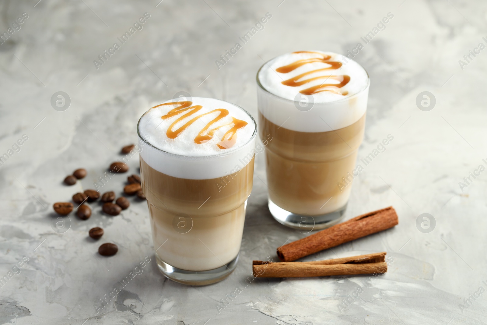 Photo of Tasty latte macchiato in glasses, coffee beans and cinnamon on grey table, closeup