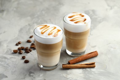 Photo of Tasty latte macchiato in glasses, coffee beans and cinnamon on grey table, closeup