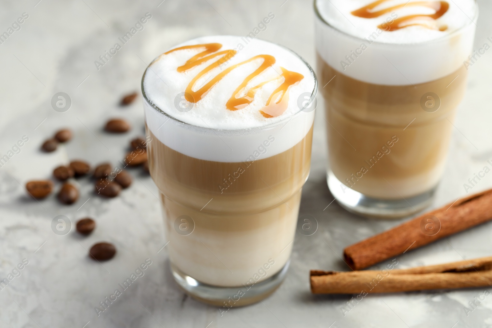 Photo of Tasty latte macchiato in glasses, coffee beans and cinnamon on grey table, closeup