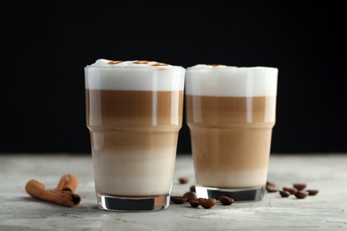 Photo of Tasty latte macchiato in glasses, coffee beans and cinnamon on grey table, closeup