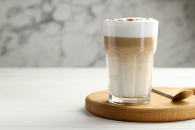 Photo of Tasty latte macchiato in glass on white wooden table, closeup. Space for text