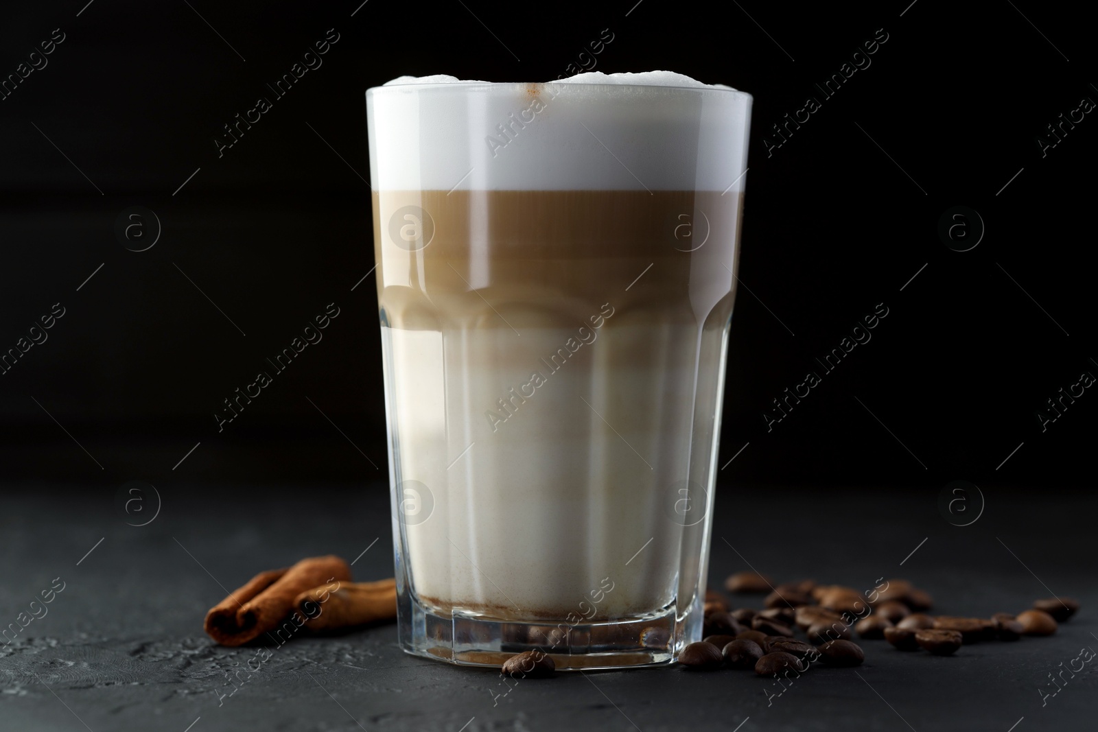 Photo of Tasty latte macchiato in glass, coffee beans and cinnamon on black table, closeup