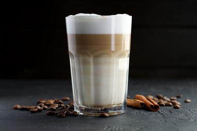 Photo of Tasty latte macchiato in glass, coffee beans and cinnamon on black table, closeup