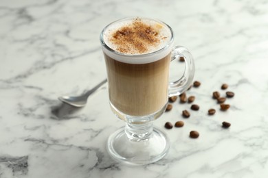 Photo of Tasty latte macchiato in glass cup and coffee beans on white marble table, closeup