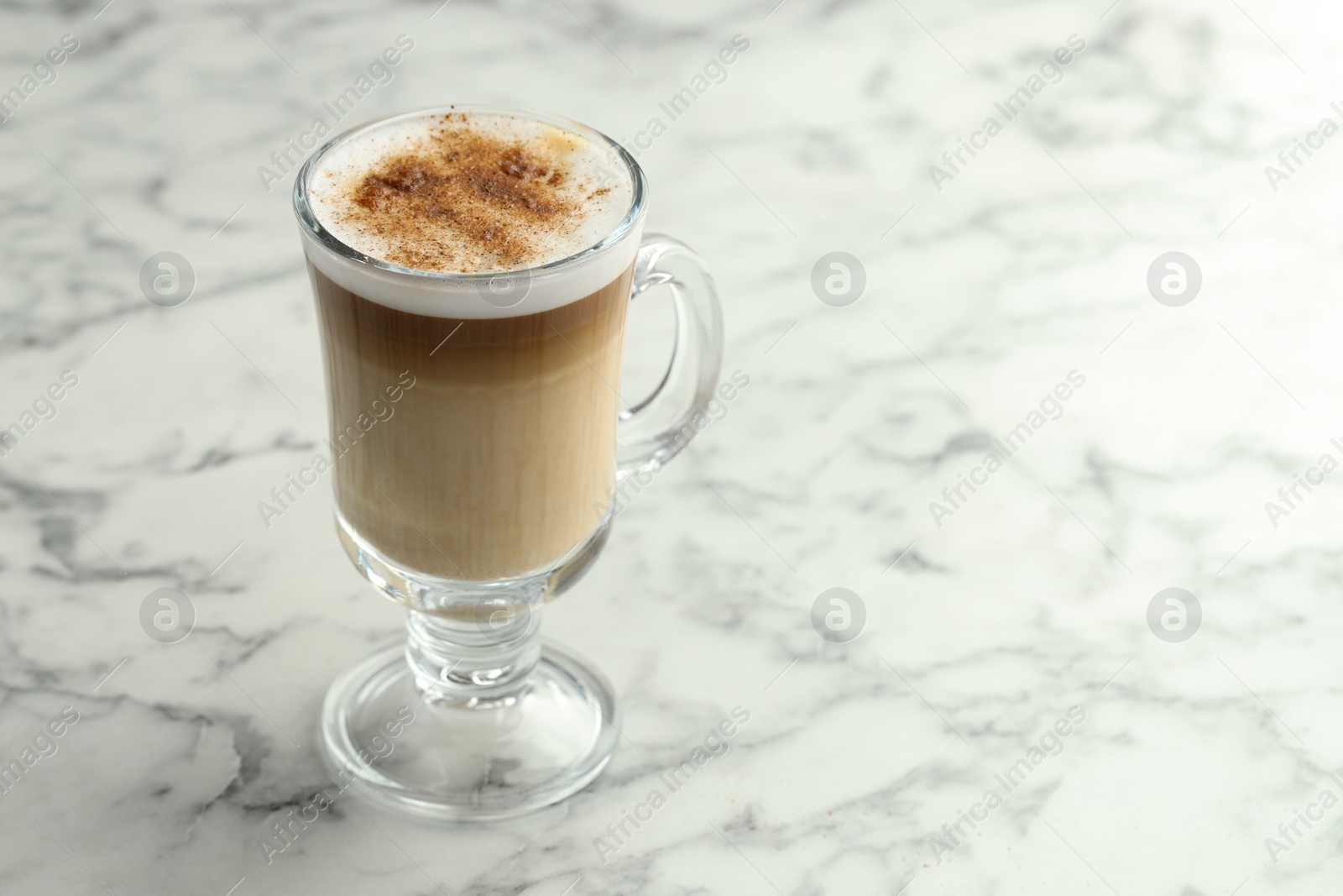 Photo of Tasty latte macchiato in glass cup on white marble table, closeup. Space for text