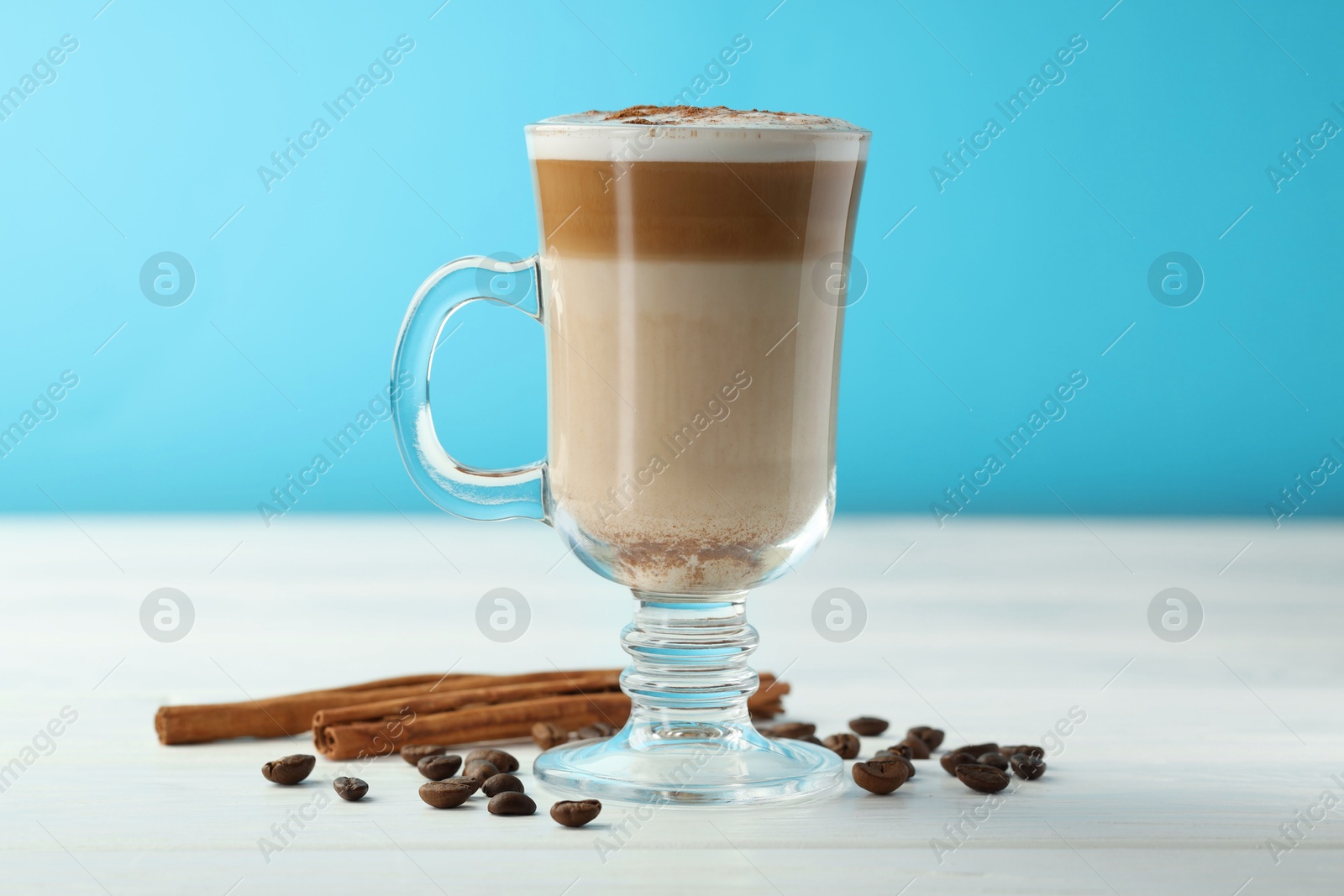 Photo of Tasty latte macchiato in glass cup, coffee beans and cinnamon on white wooden table, closeup