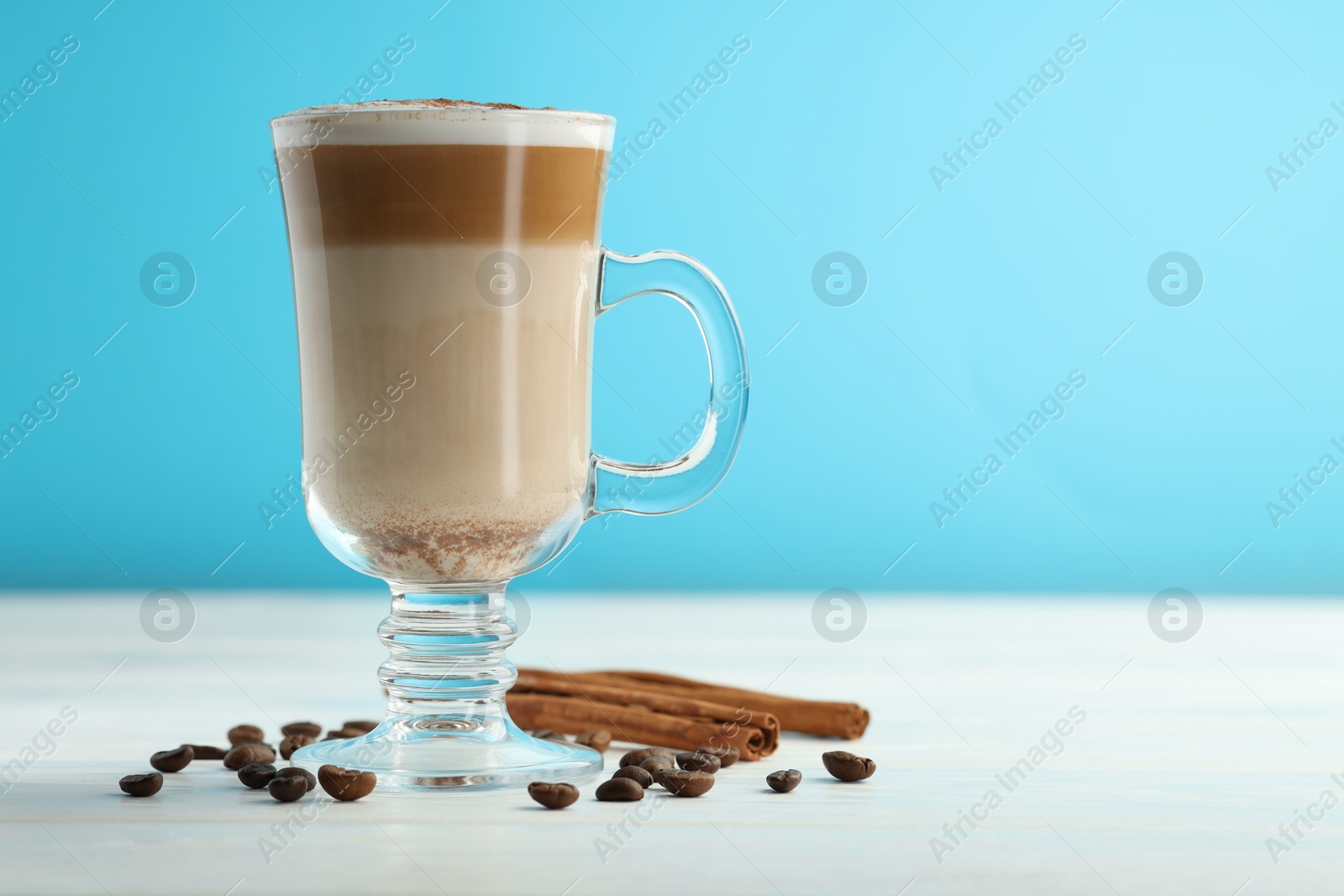 Photo of Tasty latte macchiato in glass cup, coffee beans and cinnamon on white wooden table, closeup. Space for text