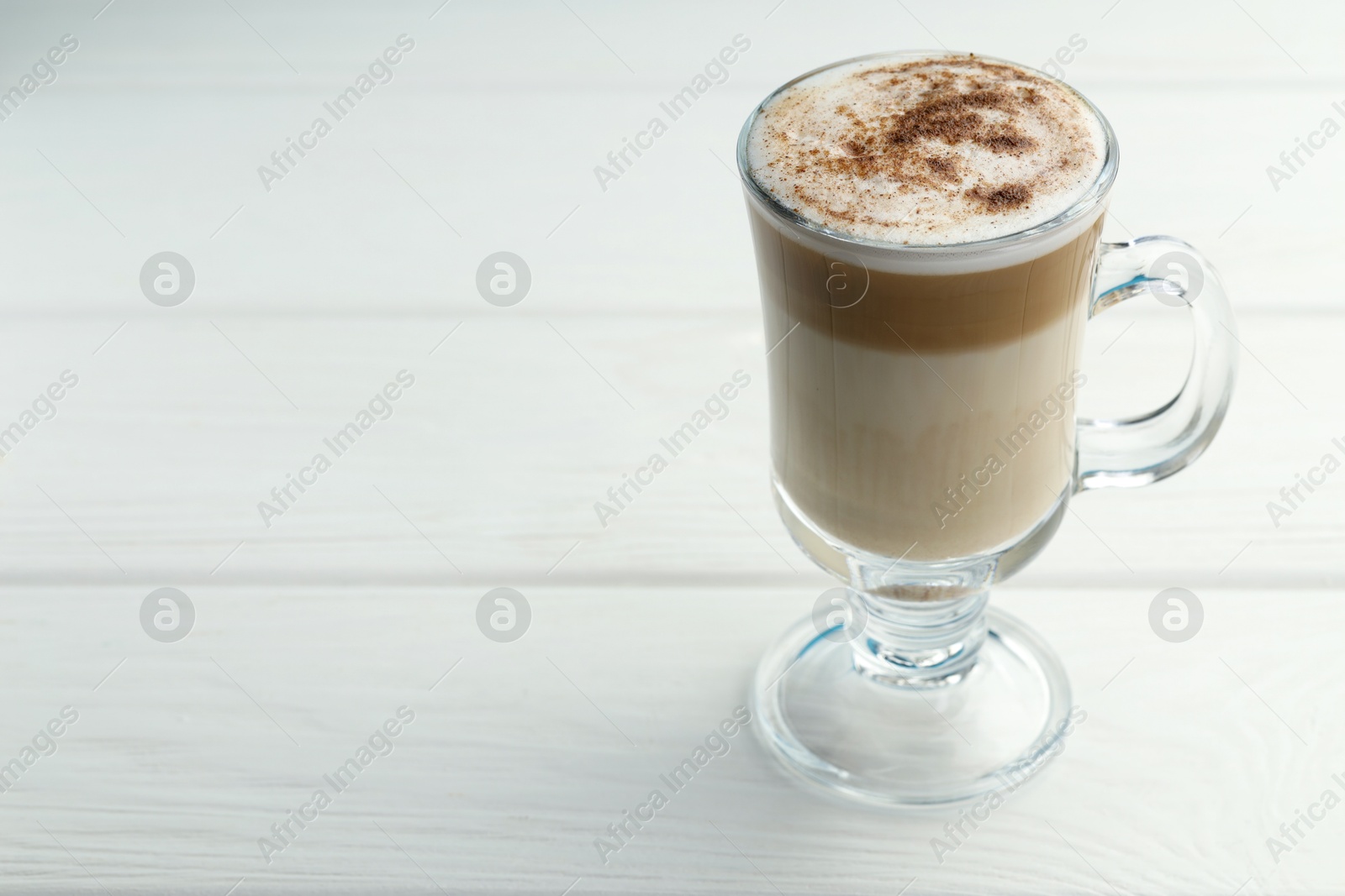 Photo of Tasty latte macchiato in glass cup on white wooden table, closeup. Space for text