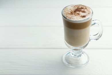 Photo of Tasty latte macchiato in glass cup on white wooden table, closeup. Space for text