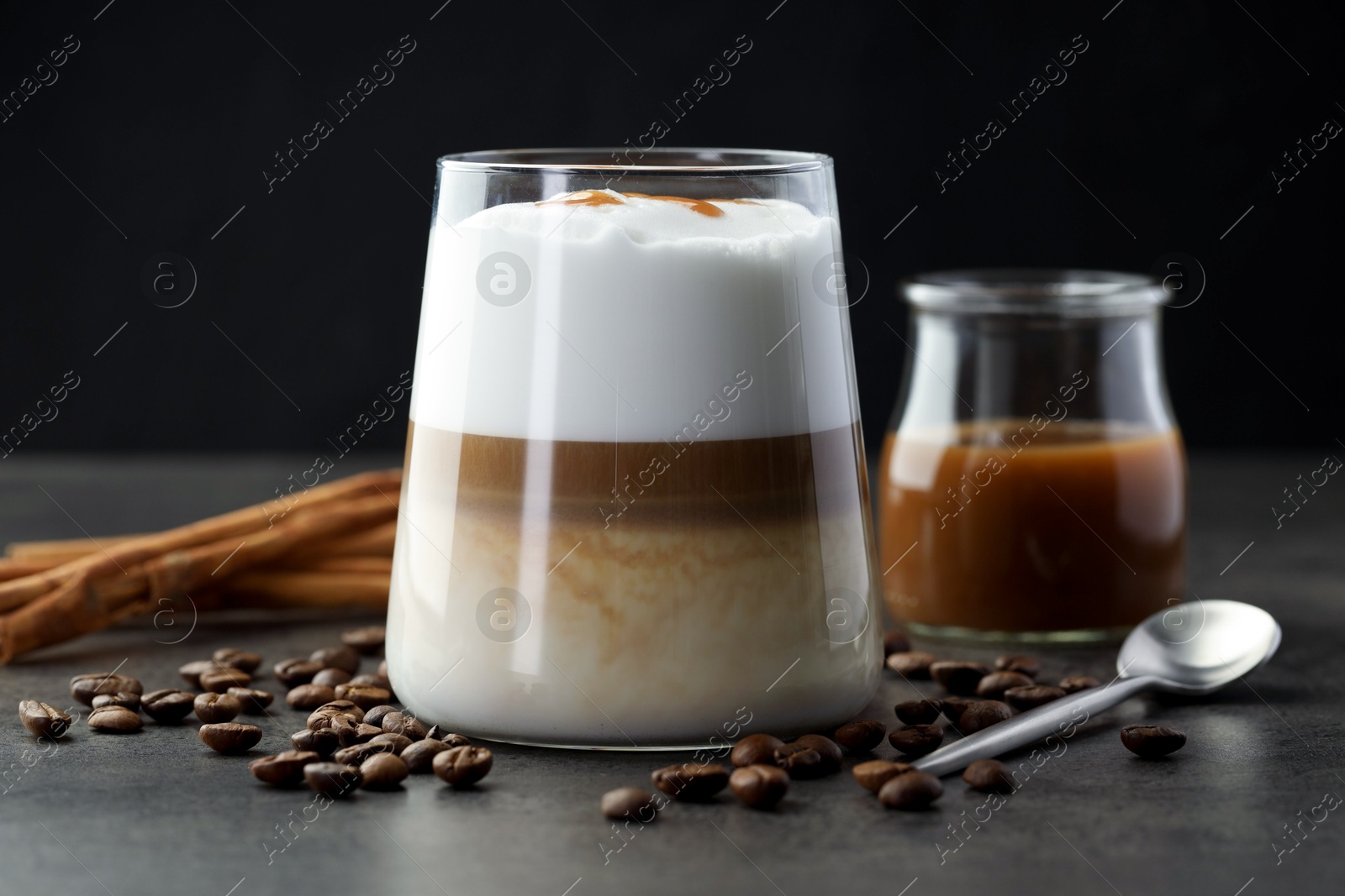 Photo of Tasty latte macchiato in glass, coffee beans and cinnamon on grey table, closeup