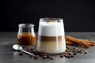 Photo of Tasty latte macchiato in glass, coffee beans and cinnamon on grey table, closeup