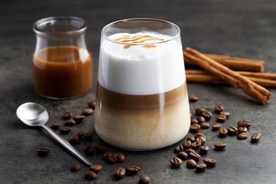 Photo of Tasty latte macchiato in glass, coffee beans and cinnamon on grey table, closeup