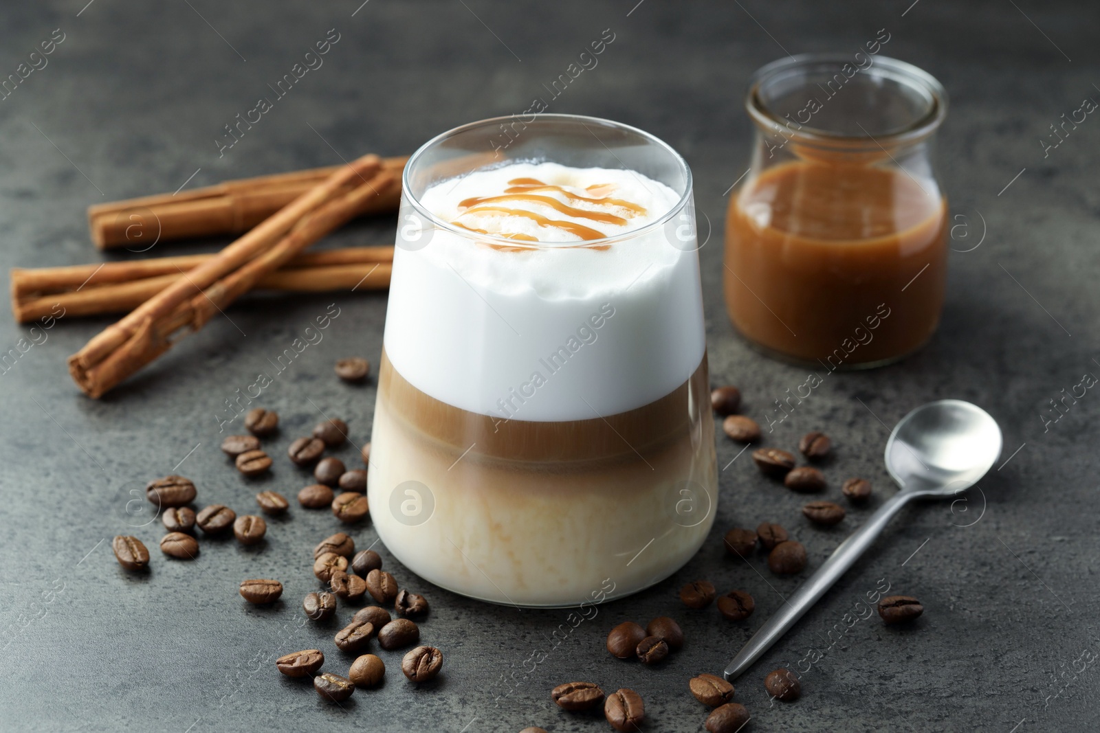 Photo of Tasty latte macchiato in glass, coffee beans and cinnamon on grey table, closeup