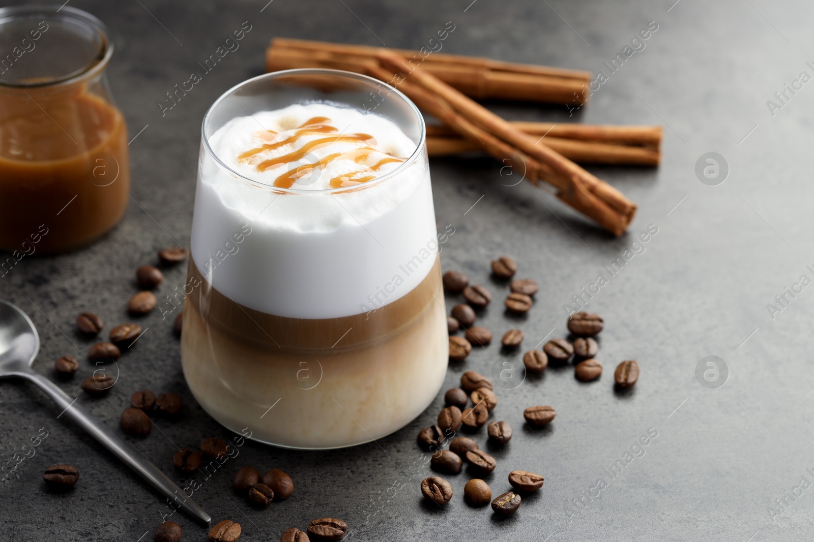 Photo of Tasty latte macchiato in glass, coffee beans and cinnamon on grey table, closeup