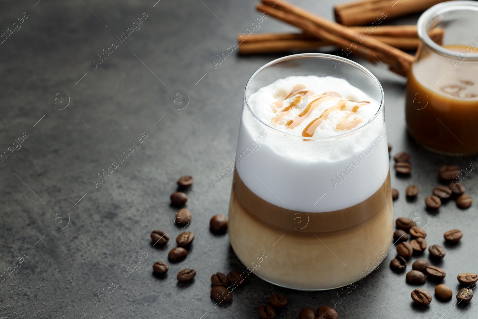 Photo of Tasty latte macchiato in glass, coffee beans and cinnamon on grey table, closeup. Space for text