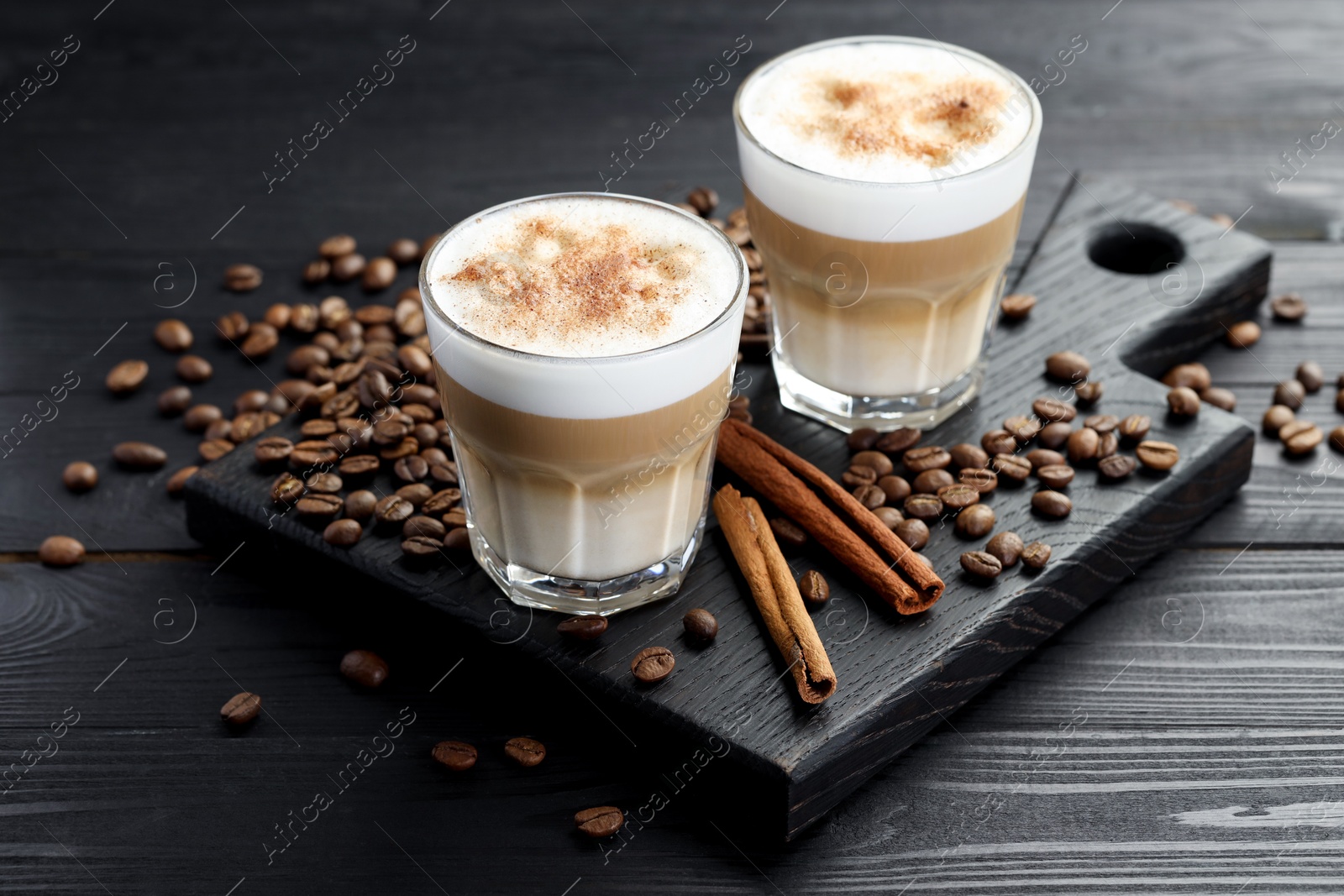 Photo of Tasty latte macchiato in glasses, coffee beans and cinnamon on black wooden table, closeup