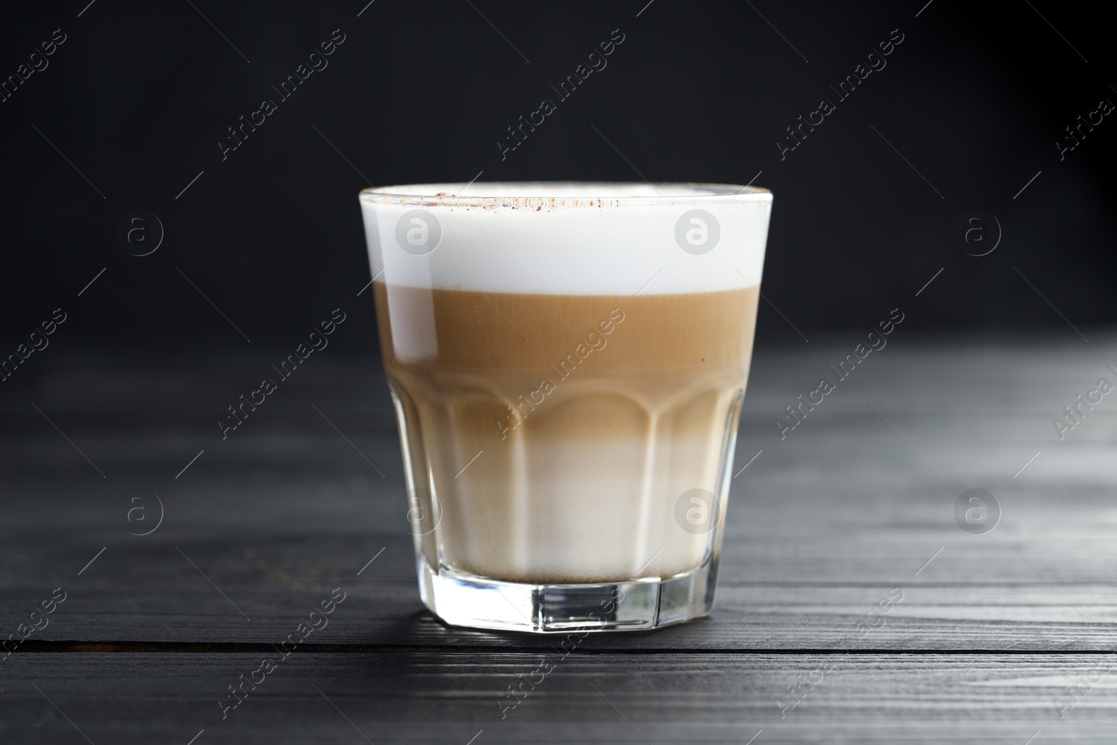 Photo of Tasty latte macchiato in glass on black wooden table, closeup