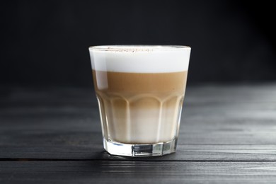 Photo of Tasty latte macchiato in glass on black wooden table, closeup