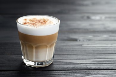 Photo of Tasty latte macchiato in glass on black wooden table, closeup. Space for text