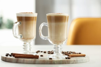 Photo of Tasty latte macchiato, coffee beans and cinnamon sticks on white table, closeup