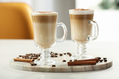 Photo of Tasty latte macchiato, coffee beans and cinnamon sticks on white table, closeup