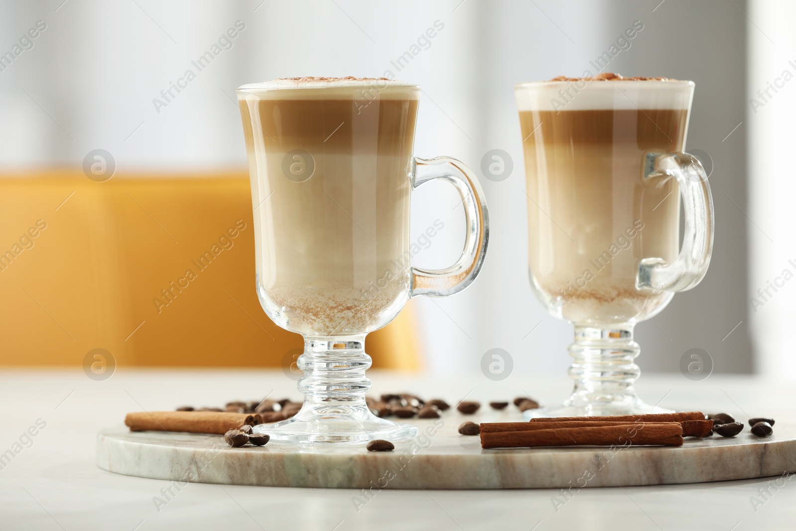 Photo of Tasty latte macchiato, coffee beans and cinnamon sticks on white table, closeup