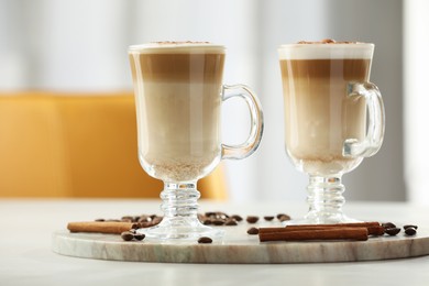 Photo of Tasty latte macchiato, coffee beans and cinnamon sticks on white table, closeup