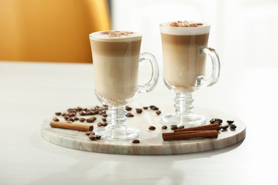 Photo of Tasty latte macchiato, coffee beans and cinnamon sticks on white table, closeup