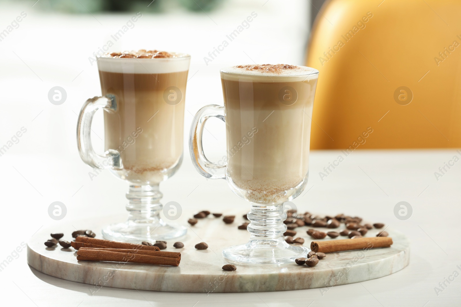 Photo of Tasty latte macchiato, coffee beans and cinnamon sticks on white table, closeup