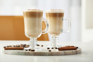 Photo of Tasty latte macchiato, coffee beans and cinnamon sticks on white table, closeup