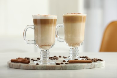 Photo of Tasty latte macchiato, coffee beans and cinnamon sticks on white table, closeup