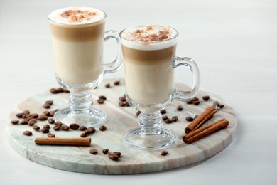 Photo of Tasty latte macchiato, coffee beans and cinnamon sticks on white table, closeup