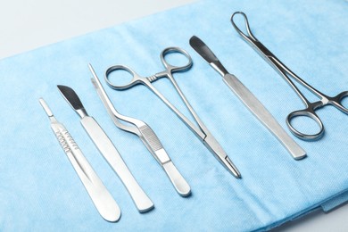 Different surgical instruments and light blue gauze on white table, closeup