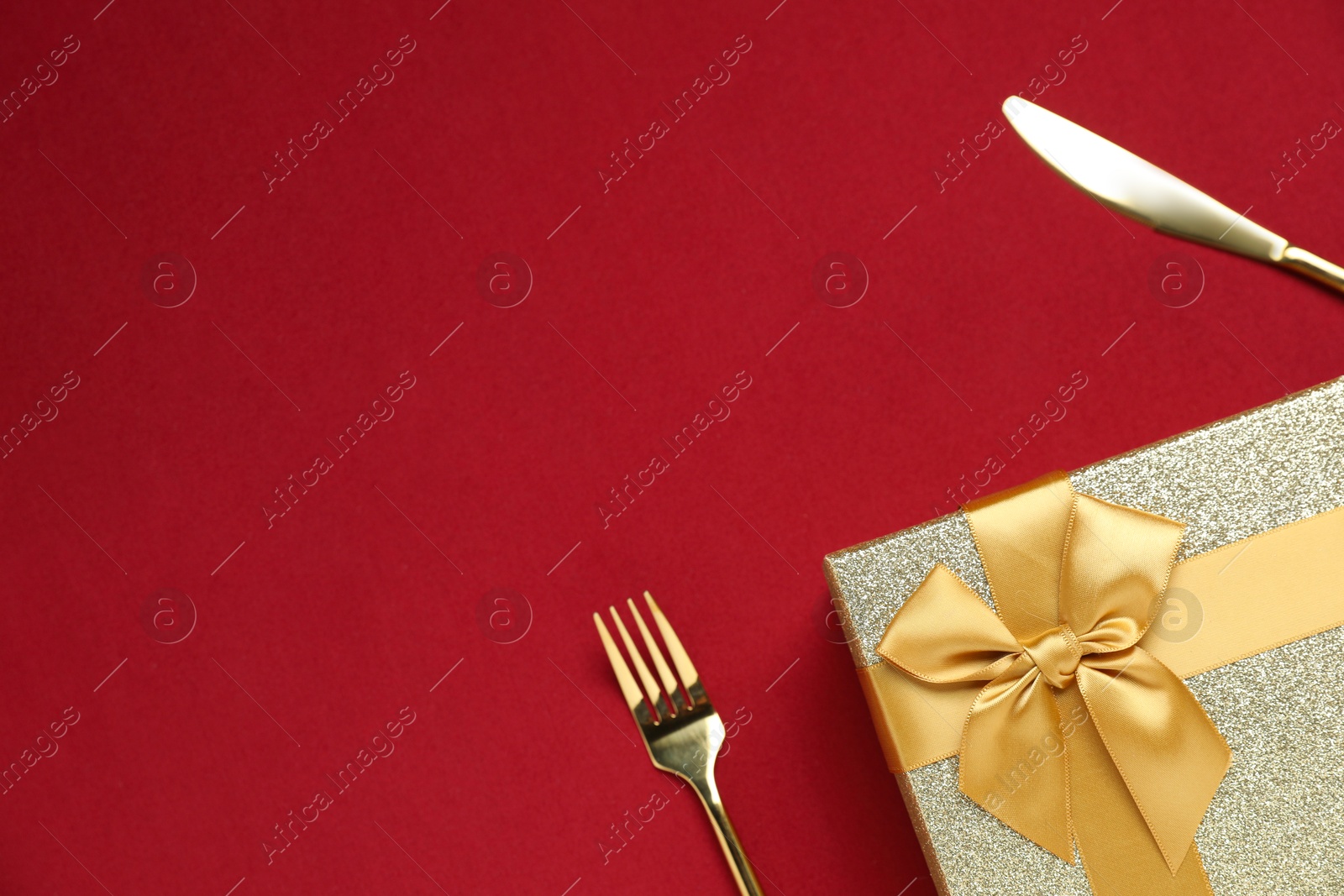 Photo of Romantic gift and cutlery on red background, top view. Space for text