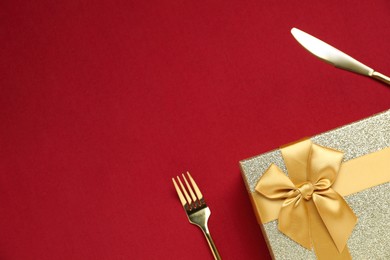 Romantic gift and cutlery on red background, top view. Space for text