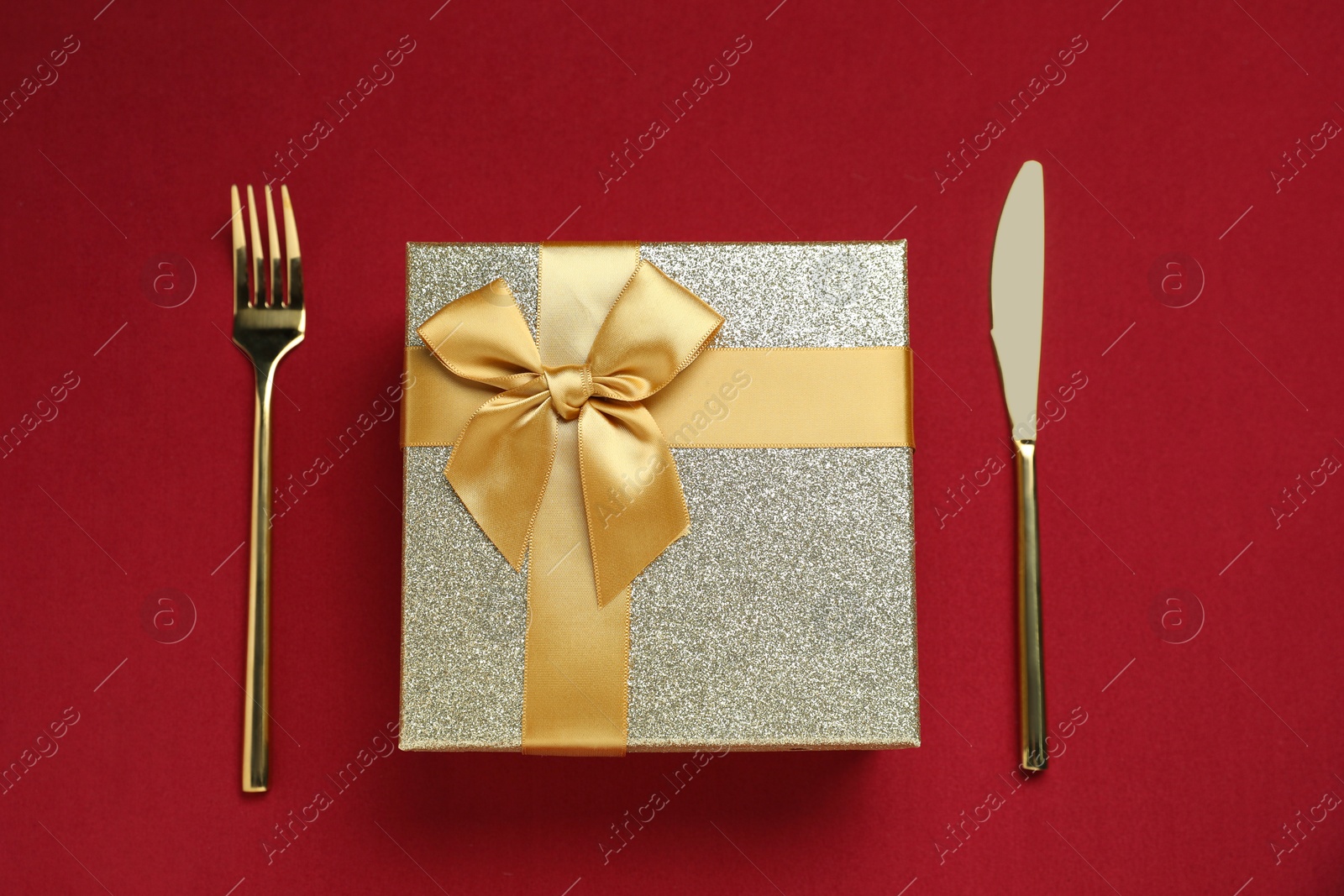 Photo of Romantic gift and cutlery on red background, top view