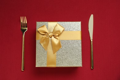 Romantic gift and cutlery on red background, top view