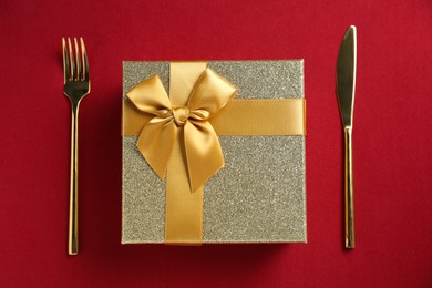 Romantic gift and cutlery on red background, top view