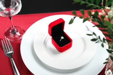 Beautiful engagement ring and setting for romantic dinner on red table, closeup