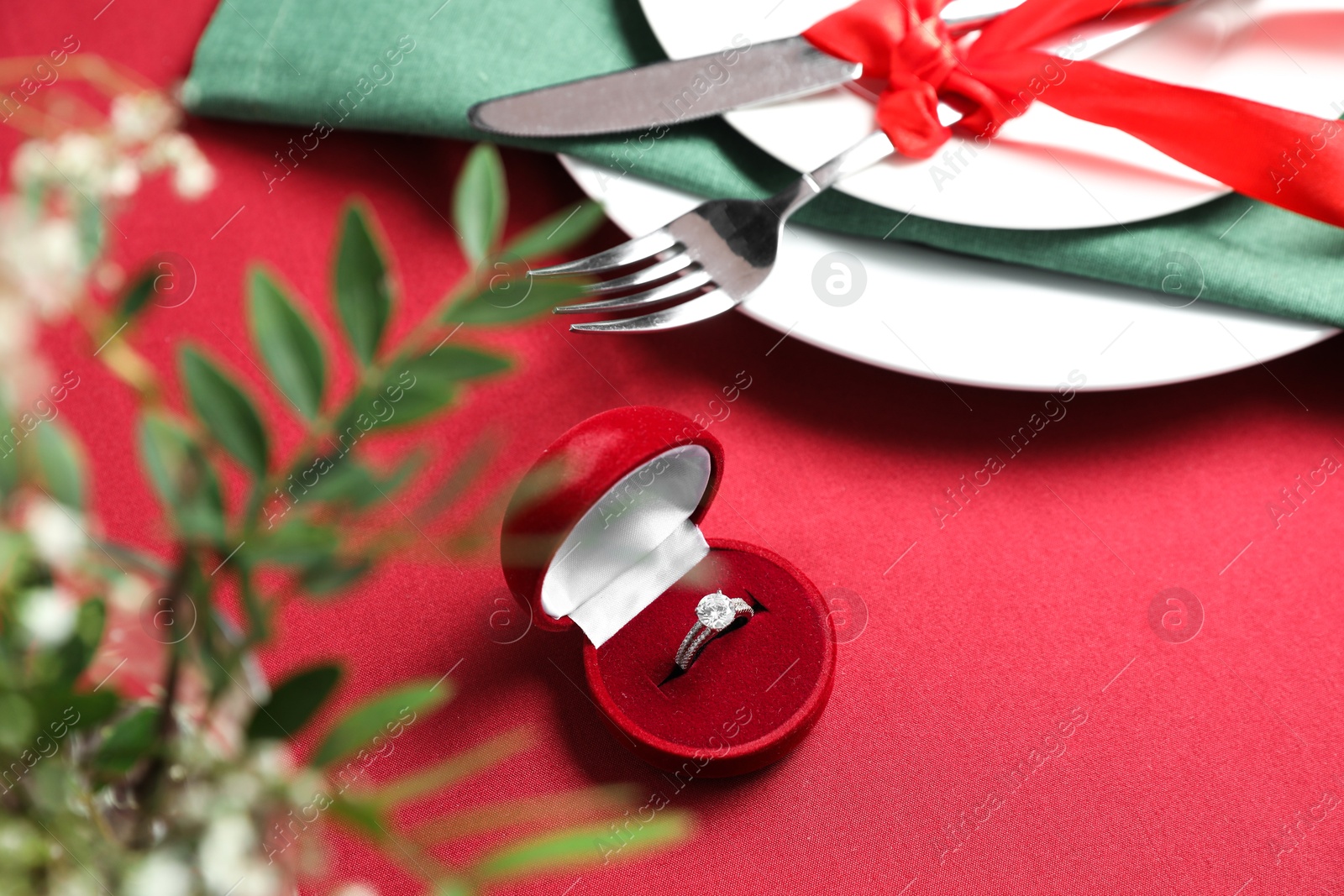 Photo of Beautiful engagement ring and setting for romantic dinner on red background, closeup