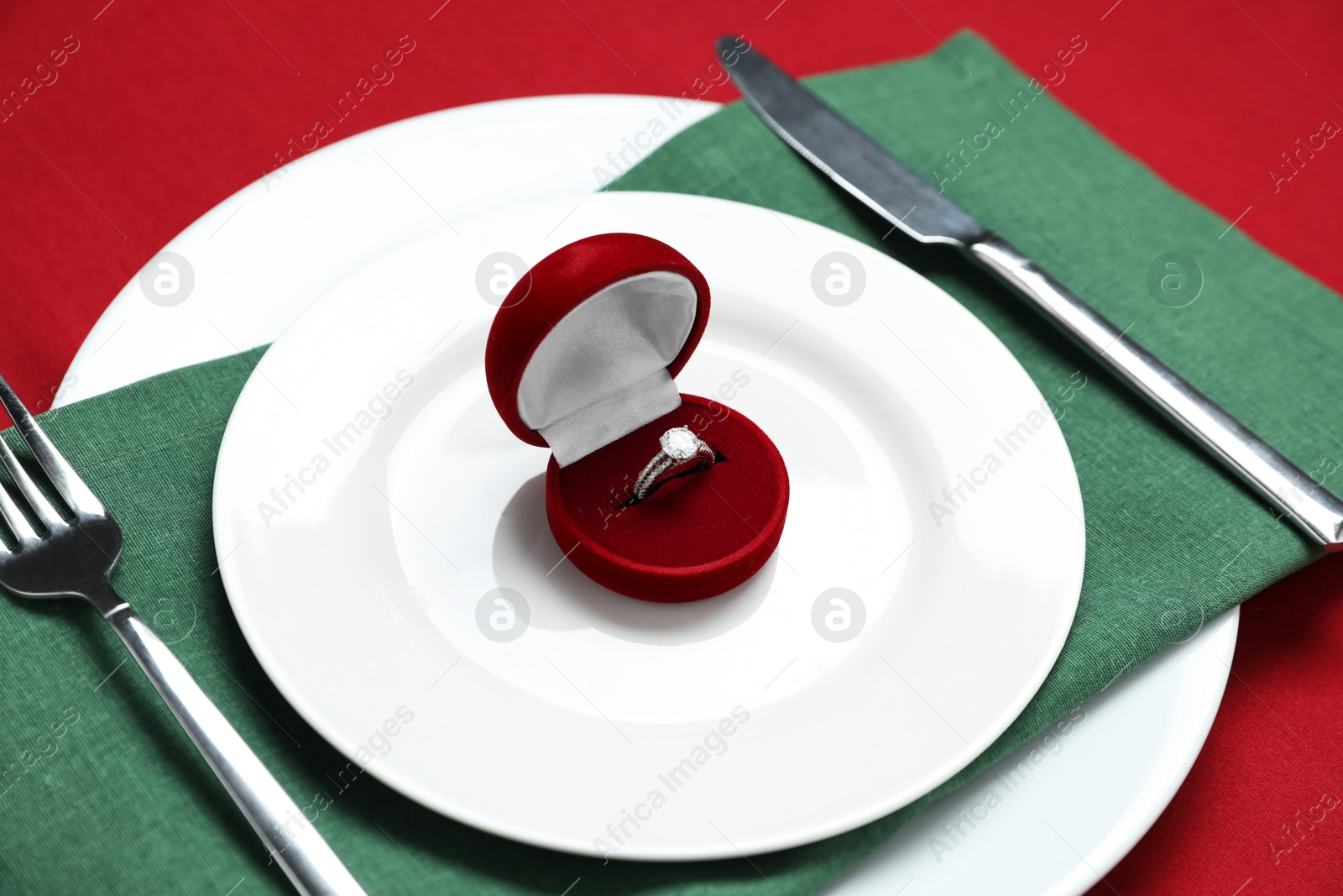 Photo of Beautiful engagement ring and setting for romantic dinner on red background, closeup