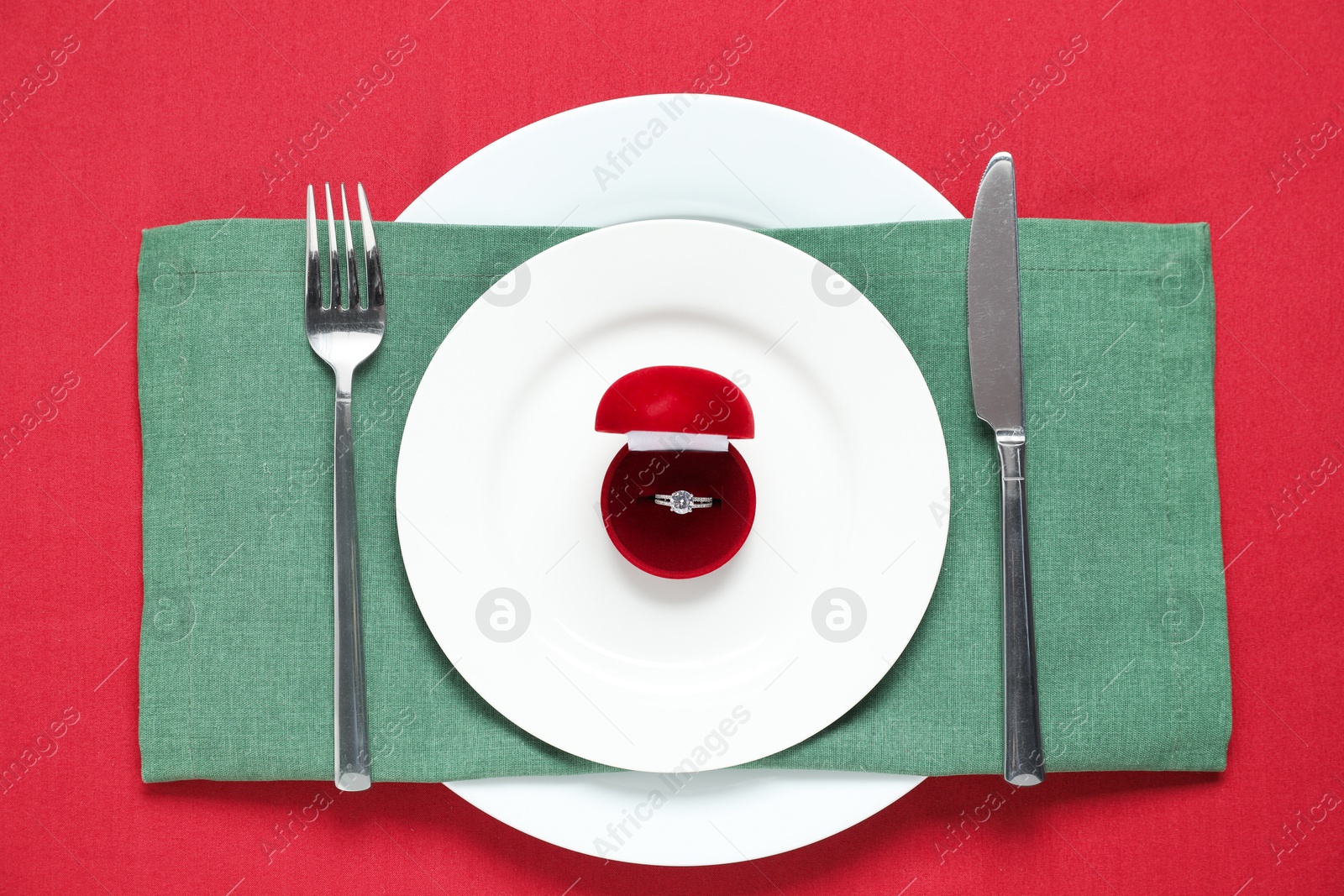 Photo of Beautiful engagement ring and setting for romantic dinner on red background, top view