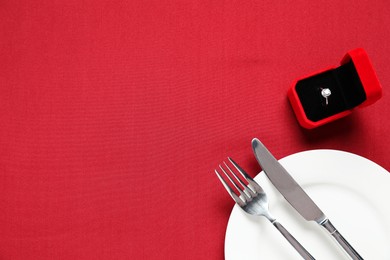 Photo of Beautiful engagement ring and setting for romantic dinner on red background, top view. Space for text