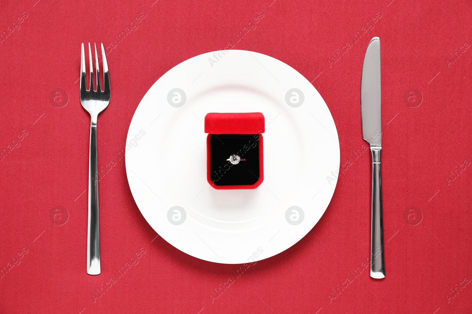 Photo of Beautiful engagement ring and setting for romantic dinner on red background, top view