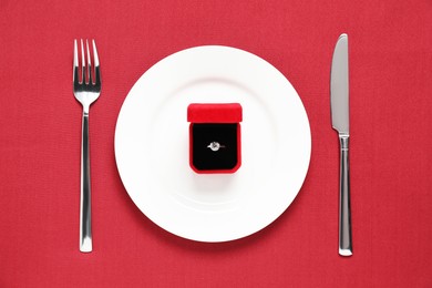 Photo of Beautiful engagement ring and setting for romantic dinner on red background, top view