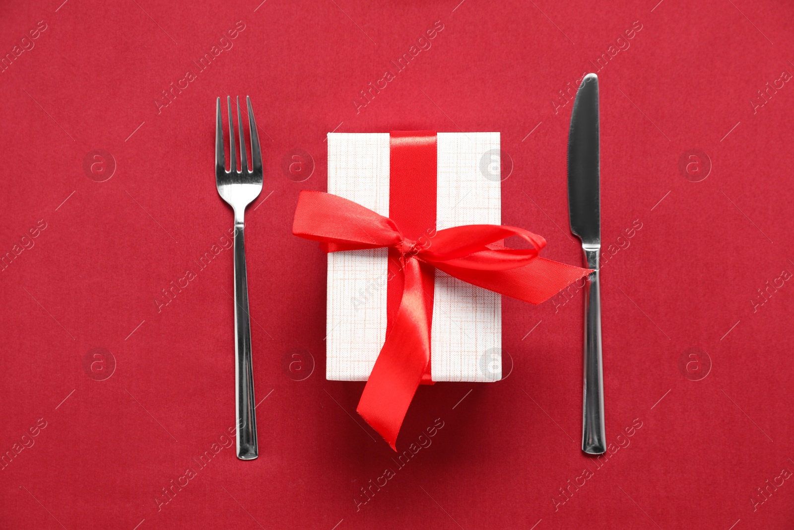 Photo of Romantic gift and cutlery on red background, top view