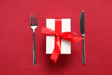 Romantic gift and cutlery on red background, top view